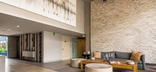 A modern lobby with a brick wall, a sofa, a coffee table, and a bookshelf. - Apartment, 2BR/2BA, AC and Heating, parking y GYM. (Ñuñoa)