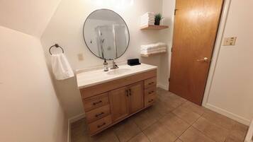 A bathroom with a wooden vanity, a round mirror, a towel rack, and a door.