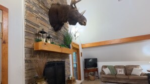 A living room with a stone fireplace, mounted deer head, and a television.