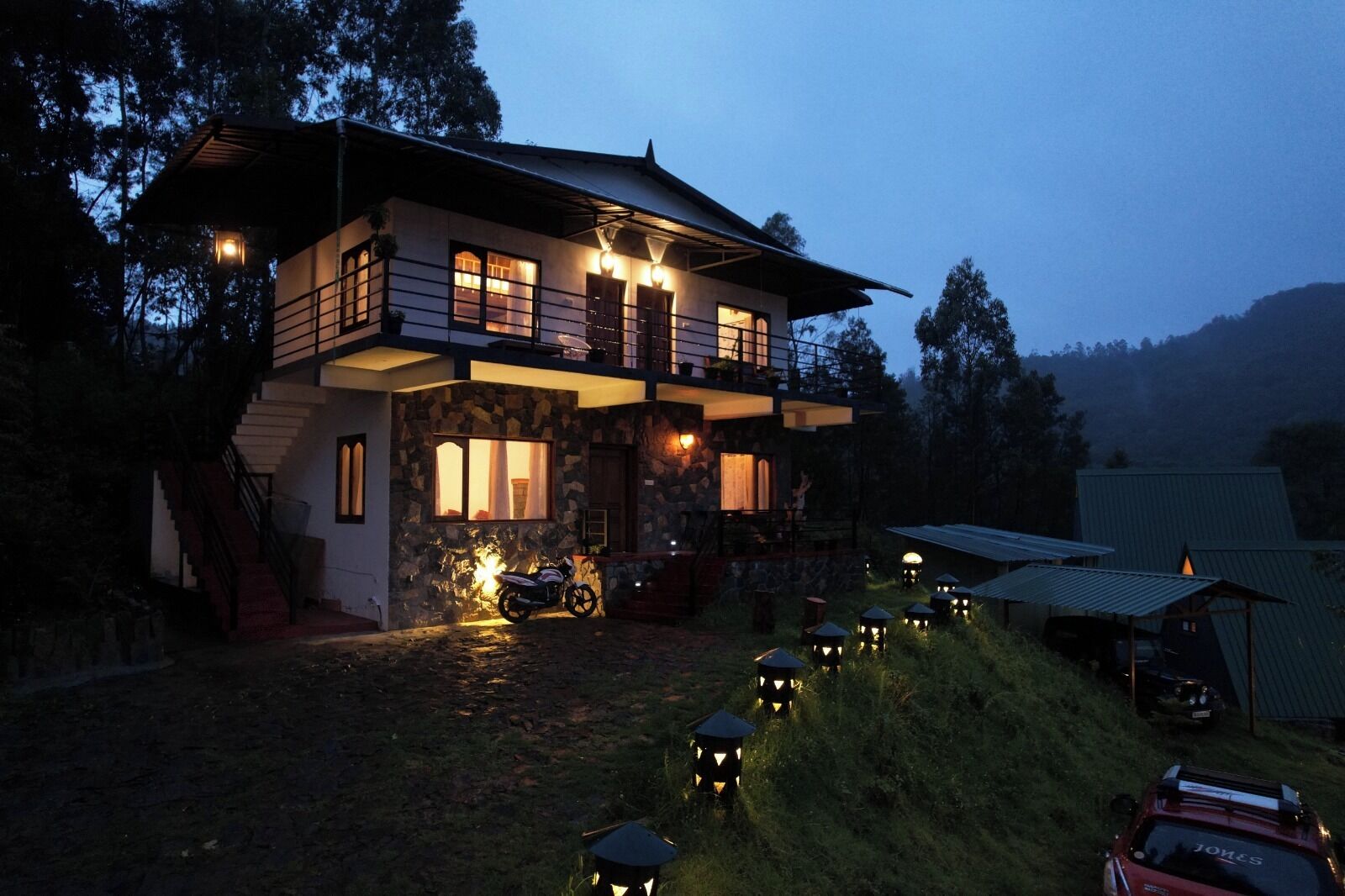 A two-story house with a stone facade, a balcony, and a driveway leading to a parked vehicle.
