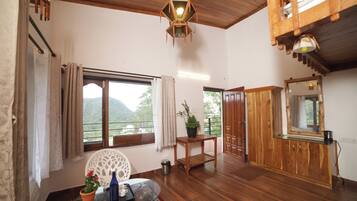 A spacious room with a wooden ceiling, a large window with a view of greenery, a wooden cabinet, and a glass table with a tray.