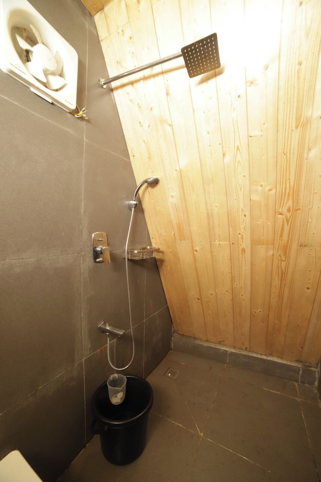 A small, enclosed bathroom with a shower, a toilet, and a bucket.