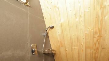 A small, enclosed bathroom with a shower, a toilet, and a bucket.