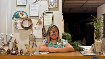 Mostrador de recepción con una mujer sentada detrás, rodeado de diversos objetos decorativos y documentos en la pared.