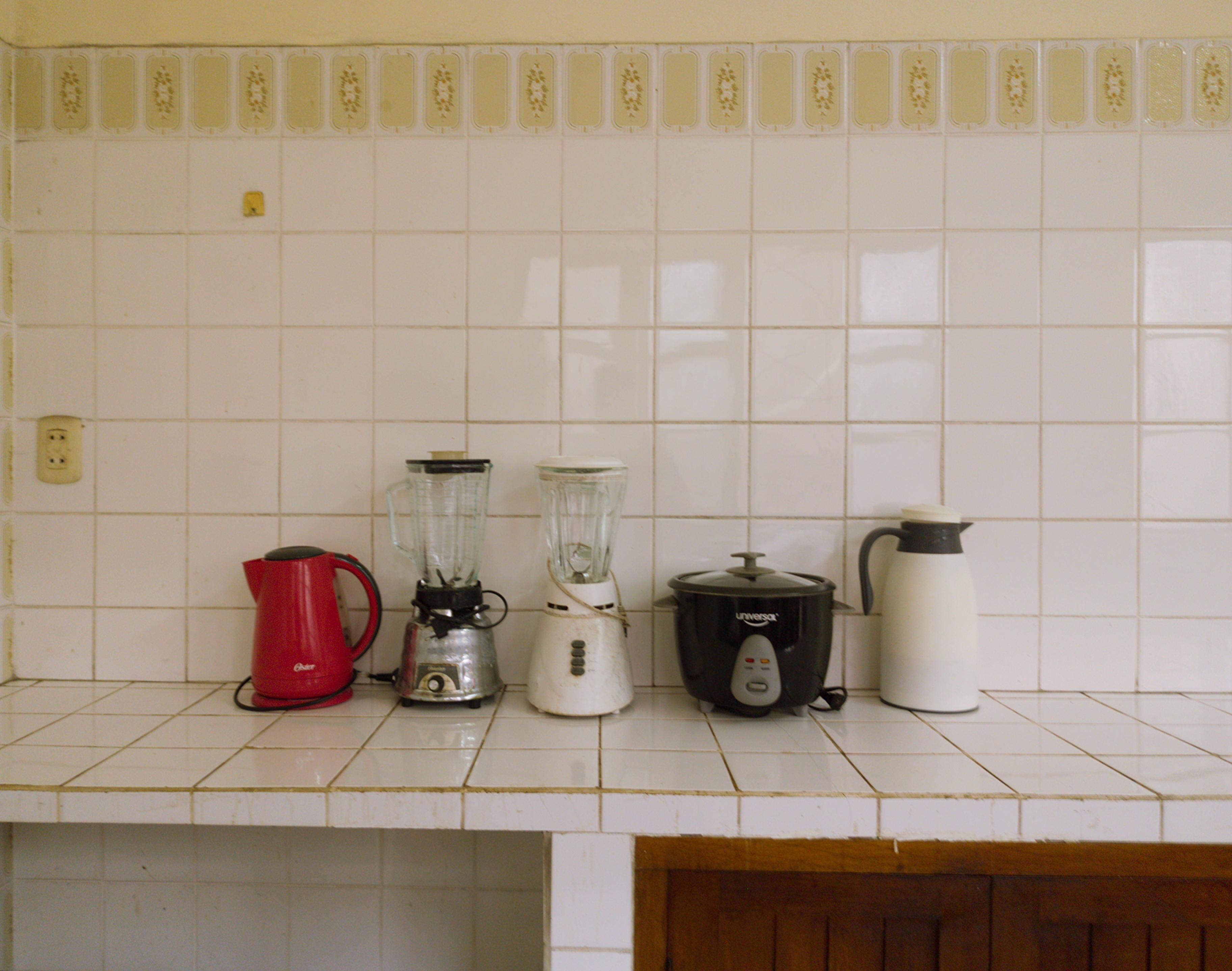 Una encimera de cocina con una tetera roja, una licuadora blanca, una olla de cocción lenta negra y una tetera eléctrica blanca.