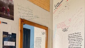 A room with a whiteboard filled with handwritten notes, a wooden door, and a small table with a plant.