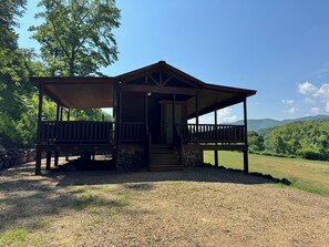 A wooden cabin with a porch, stone foundation, and a gravel ground. - Sunshine Cabin is ready to provide you with a peaceful stay! (Hot Springs)