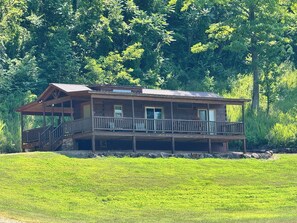 A two-story wooden cabin with a balcony, surrounded by lush greenery. - Sunshine Cabin is ready to provide you with a peaceful stay! (Hot Springs)