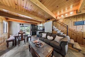 Ein gemütliches Wohnzimmer mit Holzboden, ein Essbereich mit Tisch und Stühlen, eine Küche im Hintergrund und eine Treppe mit einem Schild.