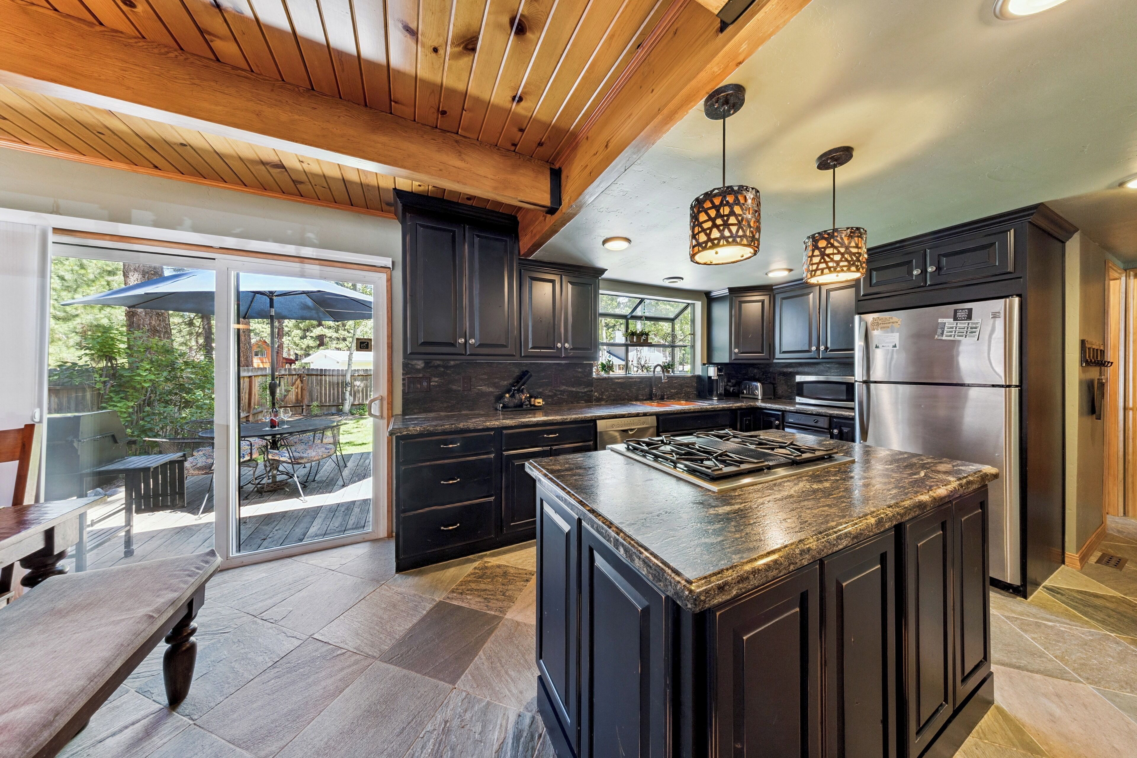 A modern kitchen with dark cabinetry, a large island, stainless steel appliances, and a view to a patio area.
