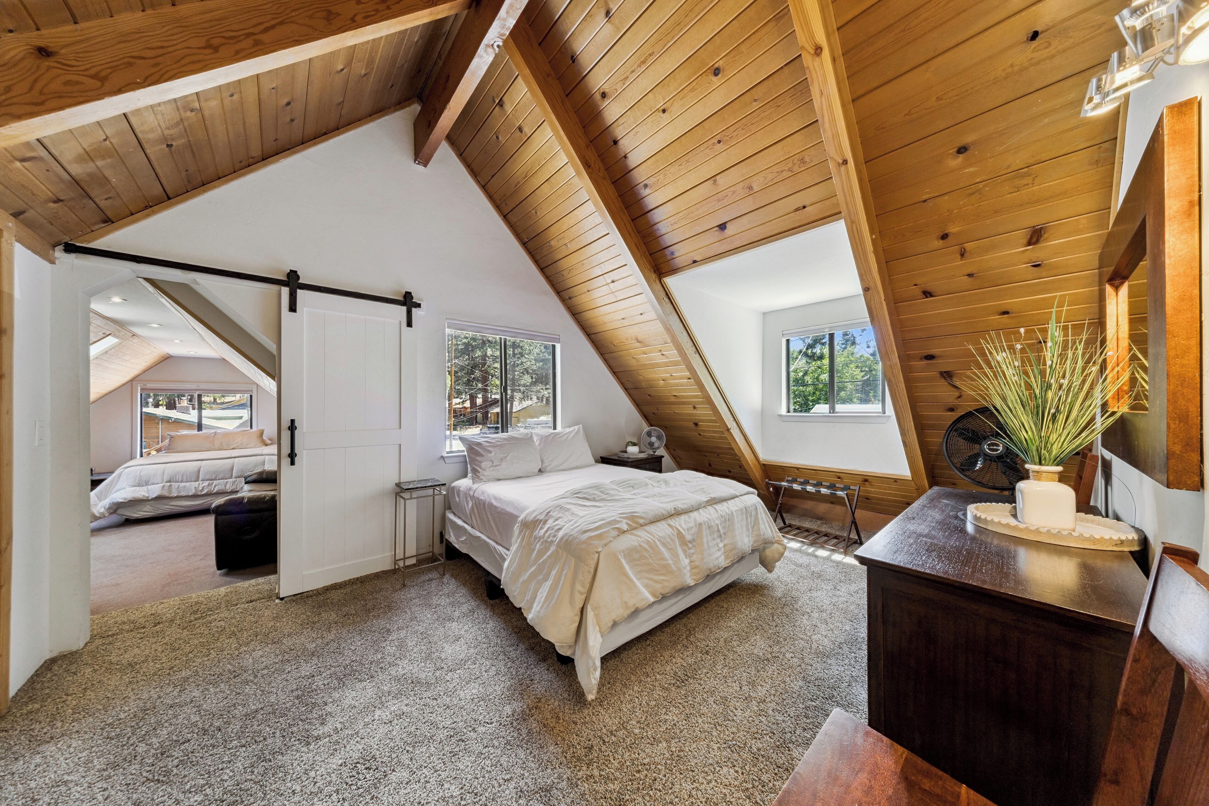 A bedroom with a sloped ceiling, a bed, a dresser, and a window.