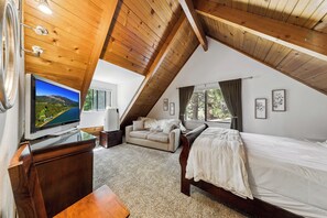 A bedroom with a sloped ceiling, a bed, a sofa, a TV, and a window with curtains. - Bear-Ski Cabin: Hot Tub, Pets, BBQ (South Lake Tahoe)