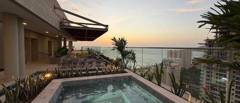 A rooftop pool area with a view of the ocean and high-rise buildings.