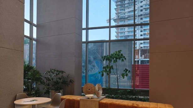 Un intérieur moderne avec une table ronde et des chaises, un banc en bois, et une vue sur un bâtiment à travers de grandes fenêtres.