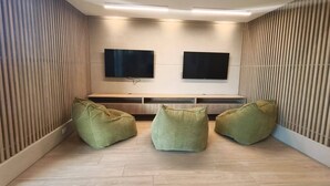 Une chambre moderne équipée de deux téléviseurs à écran plat fixés au mur, d’un banc en bois et de trois fauteuils en forme de haricot vert.