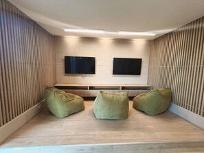 A modern room with two flat-screen TVs mounted on the wall, a wooden bench, and three green bean bag chairs. - Luxury Apartment at Bello Horizonte Beach, Santa Marta (Santa Marta)
