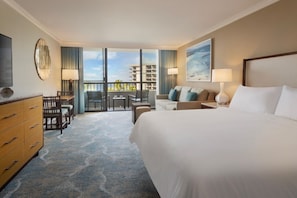 Ein Hotelzimmer mit einem großen Bett, einem Schreibtisch mit Stuhl, einer Couch, einem Fernseher und einem Balkon mit Blick auf Gebäude.