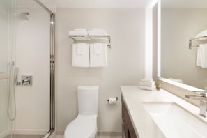 Ein modernes Badezimmer mit Duschkabine, Toilette, Waschbecken mit Spiegel und Handtuchhalter mit Handtüchern.
