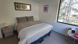 A bedroom with a bed, bedside tables, a window with a view, and wall art. - Cozy 2-bedroom apartment in serene Pucon with AC (Pucon)