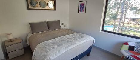 A bedroom with a bed, bedside tables, a window with a view, and wall art.