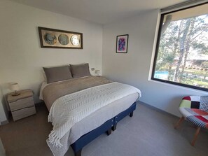 A bedroom with a bed, bedside tables, a window with a view, and wall art. - Cozy 2-bedroom apartment in serene Pucon with AC (Pucon)