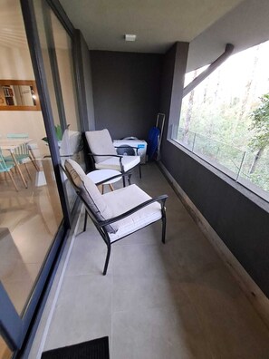 A balcony with two chairs and a table, a view of greenery outside, and a window with a metal railing. - Cozy 2-bedroom apartment in serene Pucon with AC (Pucon)