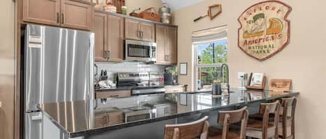 A kitchen with a central island, stainless steel appliances, wooden cabinets, and a wall-mounted sign.