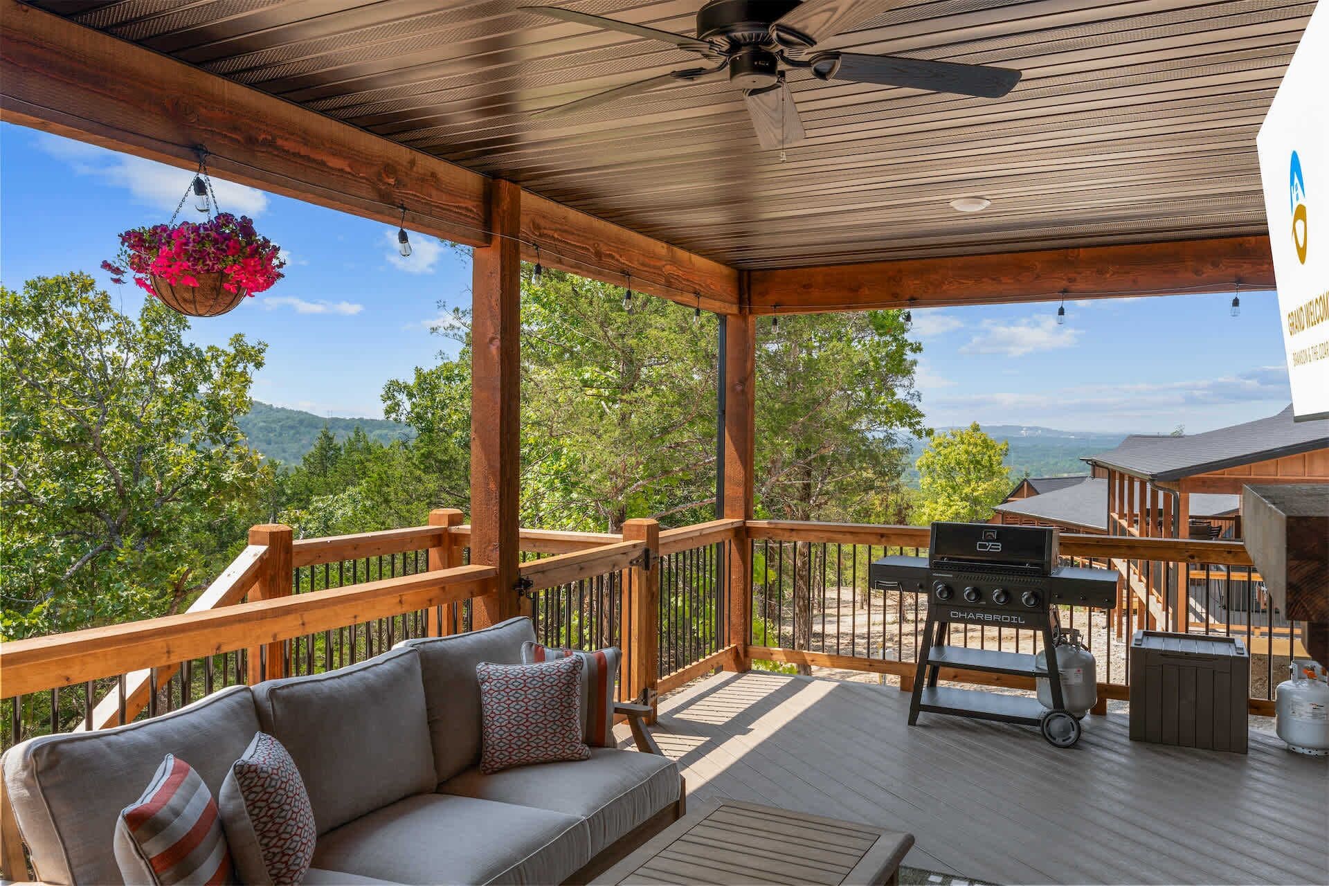 A covered outdoor deck with a sofa, a barbecue grill, and a hanging flower basket.