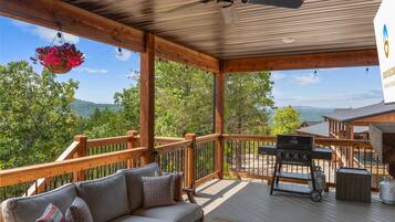 A covered outdoor deck with a sofa, a barbecue grill, and a hanging flower basket.