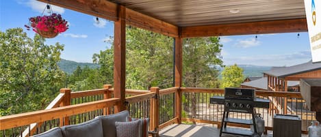 A covered outdoor deck with a sofa, a barbecue grill, and a hanging flower basket.