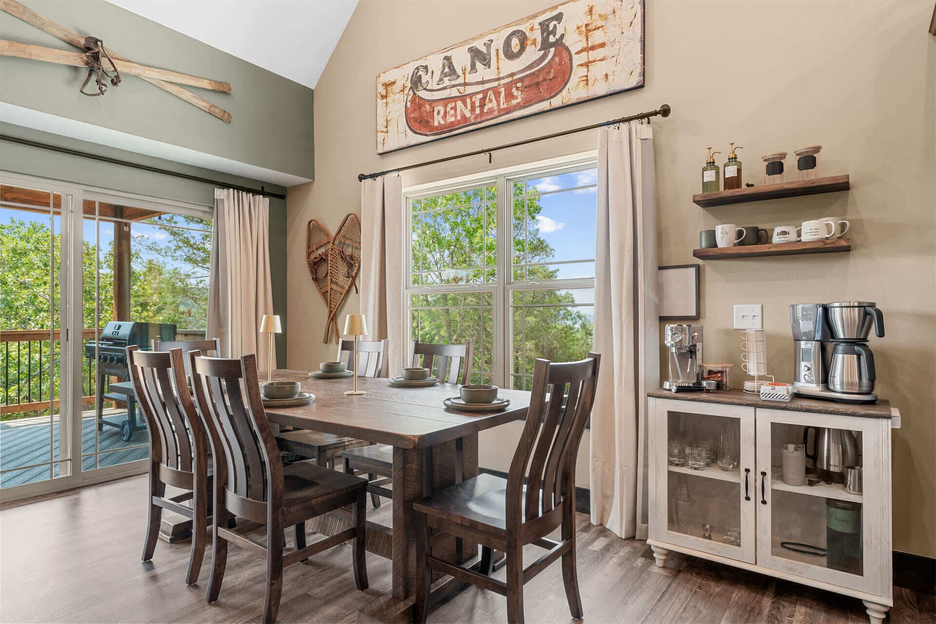 A dining area with a wooden table and chairs, a coffee station, and a view of the outdoors.
