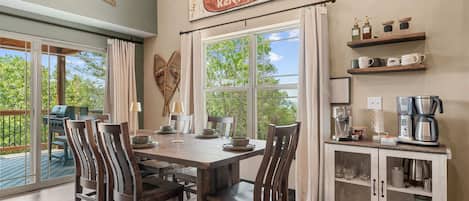 A dining area with a wooden table and chairs, a coffee station, and a view of the outdoors.