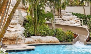 Una piscina con una formación rocosa y palmeras.