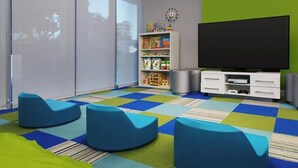 Quarto com uma televisão de tela grande, estante de brinquedos e assentos acolchoados azuis.