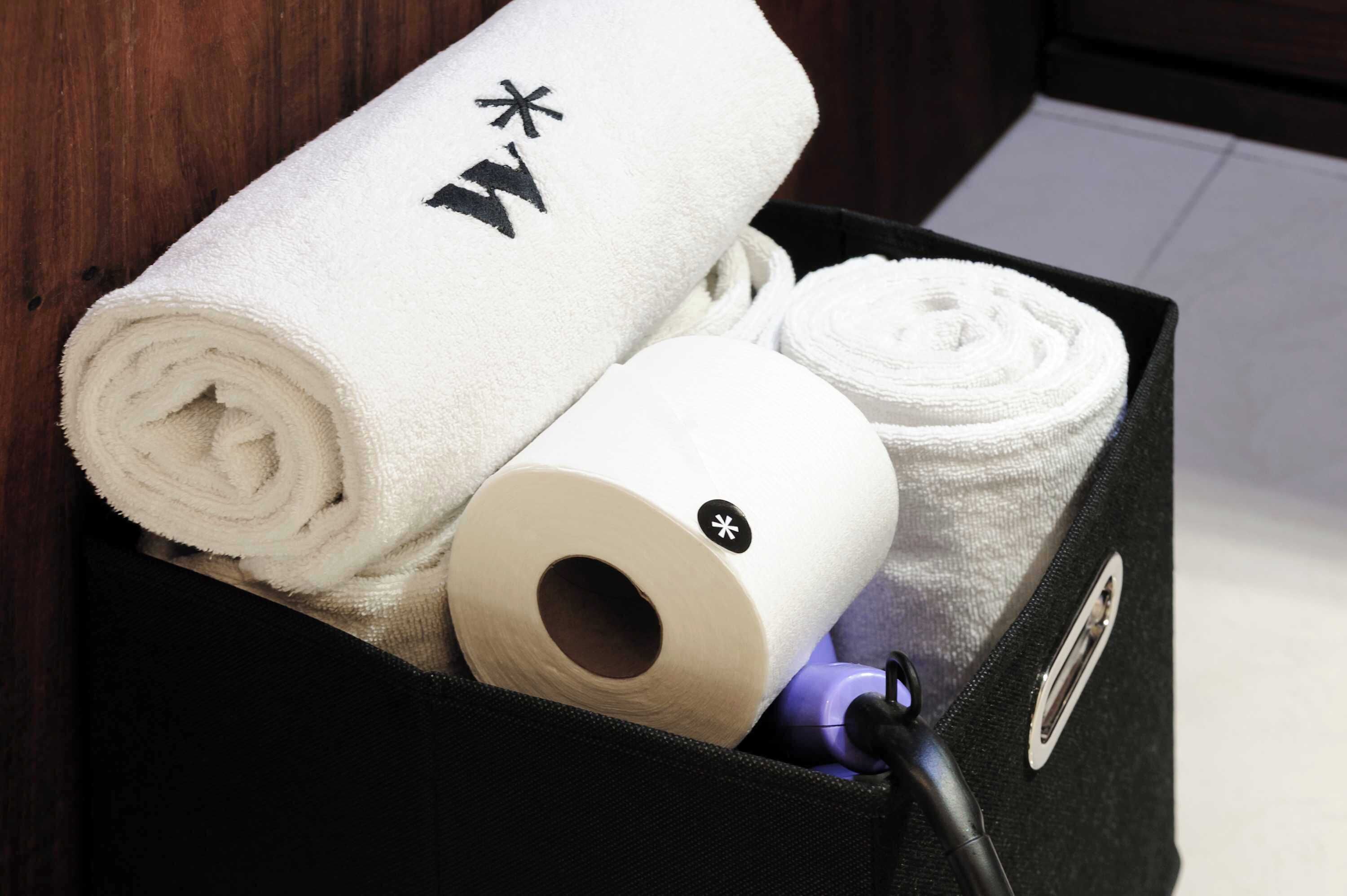 Une boîte noire contenant des serviettes blanches roulées, ornées d’un symbole noir, ainsi qu’une serviette blanche avec un bouton noir.