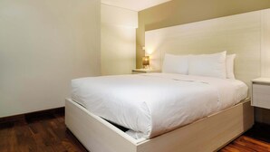 Un lit bien fait dans une chambre d’hôtel, avec une tête de lit en bois, une table de chevet avec une lampe et un plancher en bois.