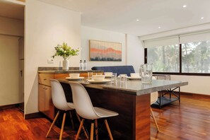 A modern kitchen with a central island, white chairs, and a dining area with a blue sofa. - w* | Amazing 1BR in Prime Polanco (Ciudad de México)