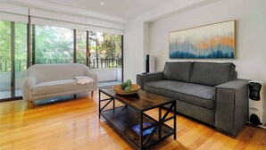 Ein modernes Wohnzimmer mit einem grauen Sofa, einem Holztisch und einem großen abstrakten Gemälde an der Wand.
