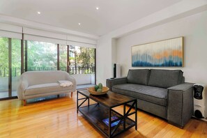A modern living room with a grey sofa, a wooden coffee table, and a large abstract painting on the wall. - w* | Deluxe 1BR  Duplex in Prime Polanco (Ciudad de México)