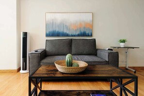 A modern living room with a grey sofa, a coffee table with a woven basket, a tall air purifier, and a painting on the wall. - w* | Deluxe 1BR Duplex in Polanco (Ciudad de México)