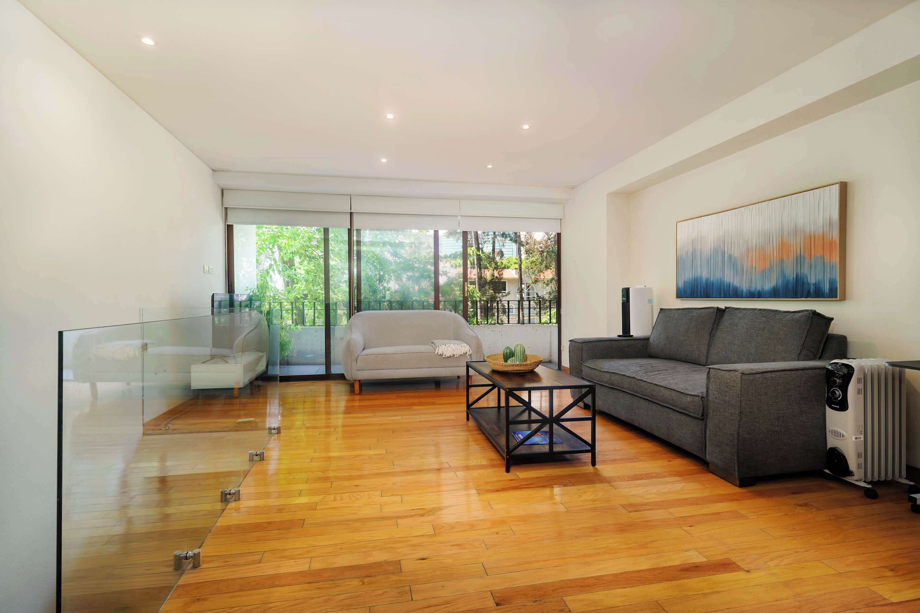A modern living room with a glass partition, a grey sofa, a wooden coffee table, and a radiator.