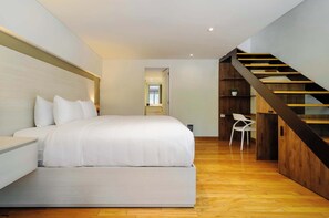 A modern bedroom with a large bed, a wooden staircase, and a white chair. - w* | Deluxe 1BR  Duplex in Prime Polanco (Ciudad de México)