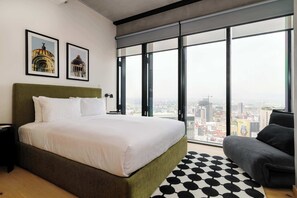 Ein modernes Hotelzimmer mit einem großen Bett, Blick auf die Stadt und zwei gerahmten Bildern an der Wand.