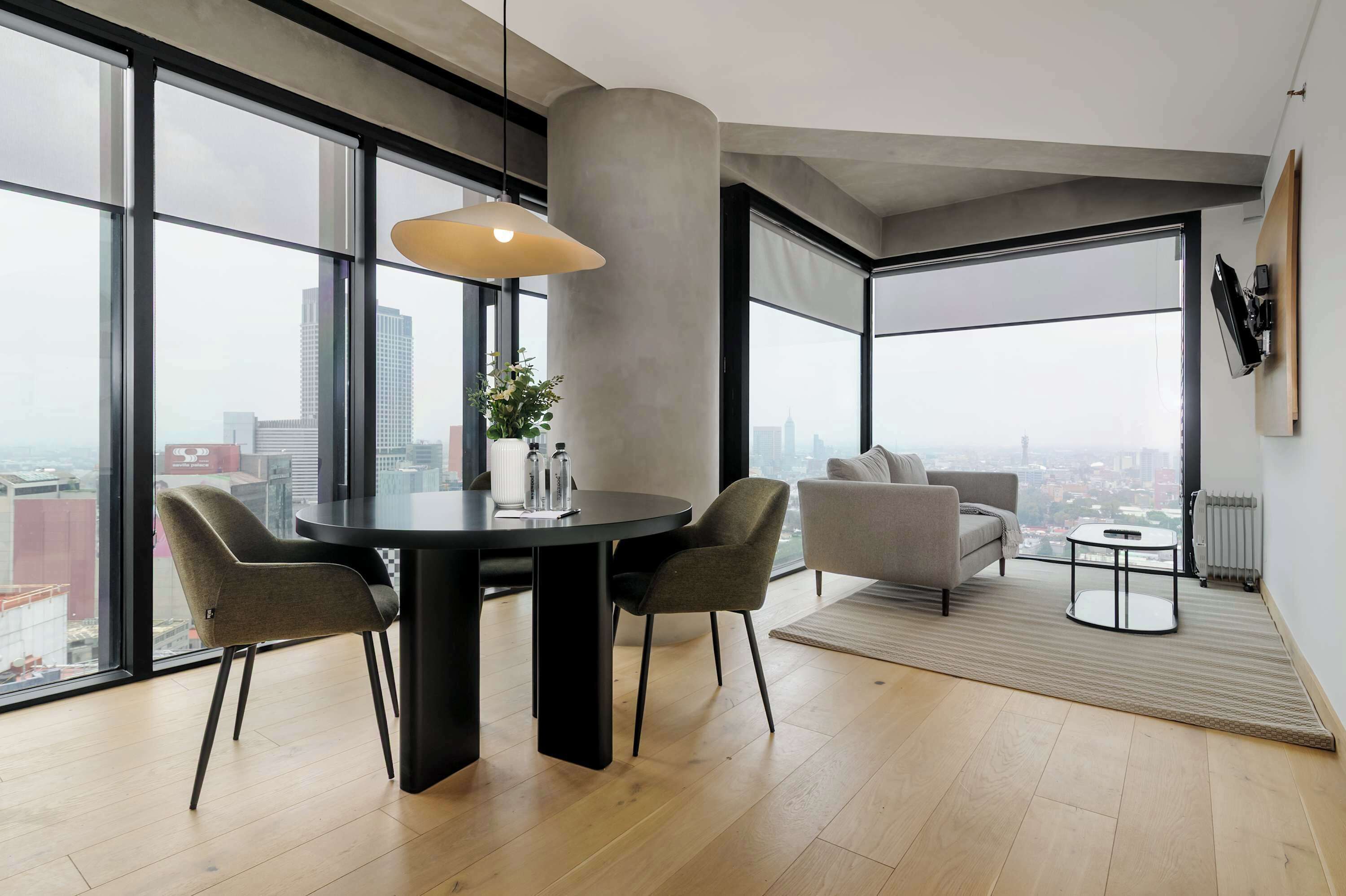Una sala moderna con una mesa redonda, dos sillas, un sofá y un ventanal con vistas a la ciudad.