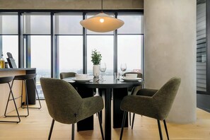 A modern dining area with a round table, four chairs, a hanging light fixture, and a city view through large windows. - w* | Stylish 1BR in Juarez (Ciudad de México)