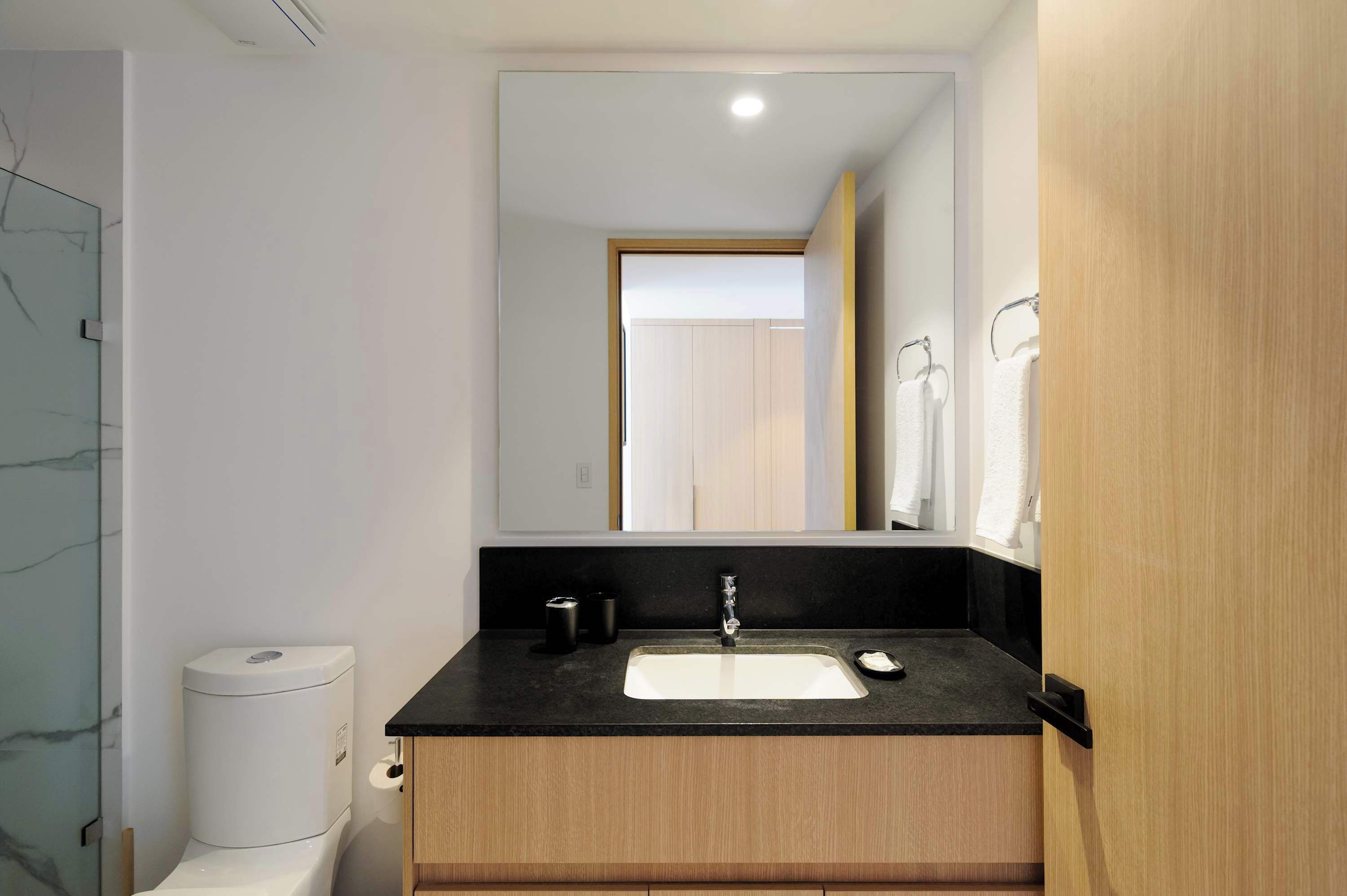 Een moderne badkamer met een zwart aanrecht, een witte wastafel en een spiegel erboven.