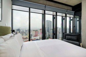 A modern hotel room with a large bed, a chair, and a city view through floor-to-ceiling windows. - w* | Stylish 1BR in Juarez (Ciudad de México)