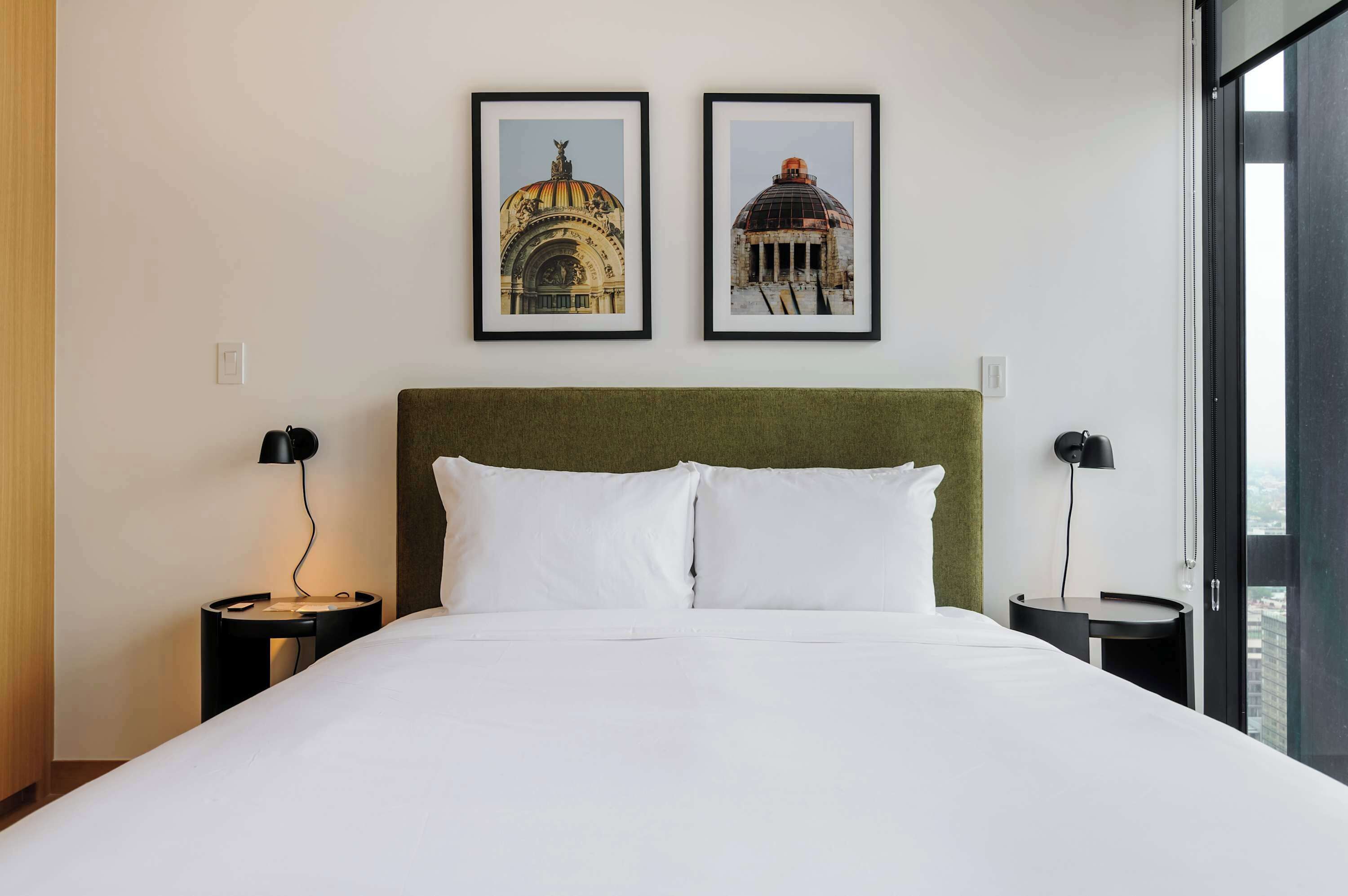 Une chambre d’hôtel avec un grand lit, deux tables de chevet, une tête de lit verte et deux tableaux encadrés accrochés au mur.