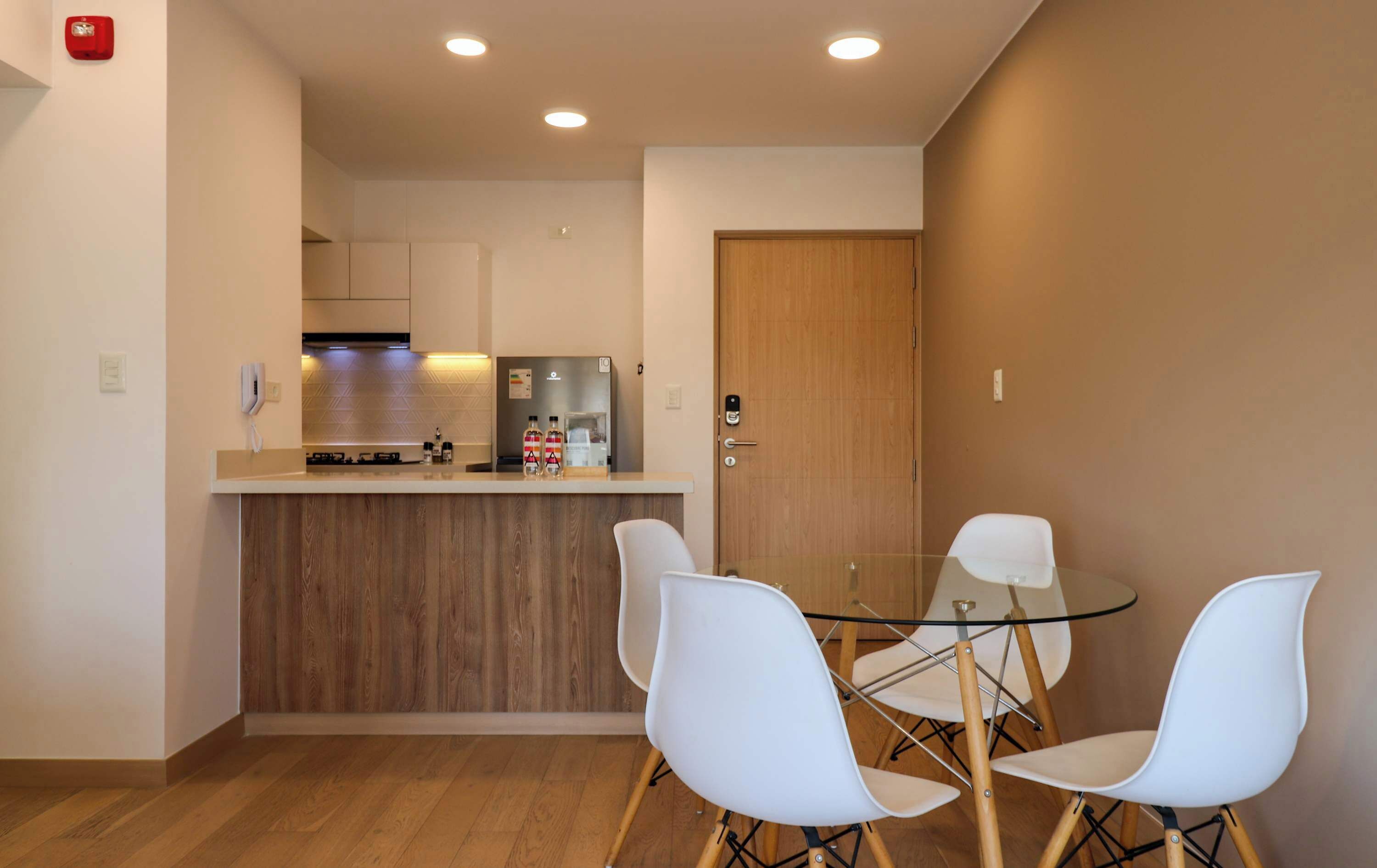 A compact kitchen with a wooden countertop, a sink, and a stove. There are two white chairs around a glass table.