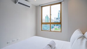 A hotel room with a bed, a window with a city view, an air conditioning unit, and electrical outlets. - w* | Upscale 1BR in Obarrio w/ AC (Panamá)